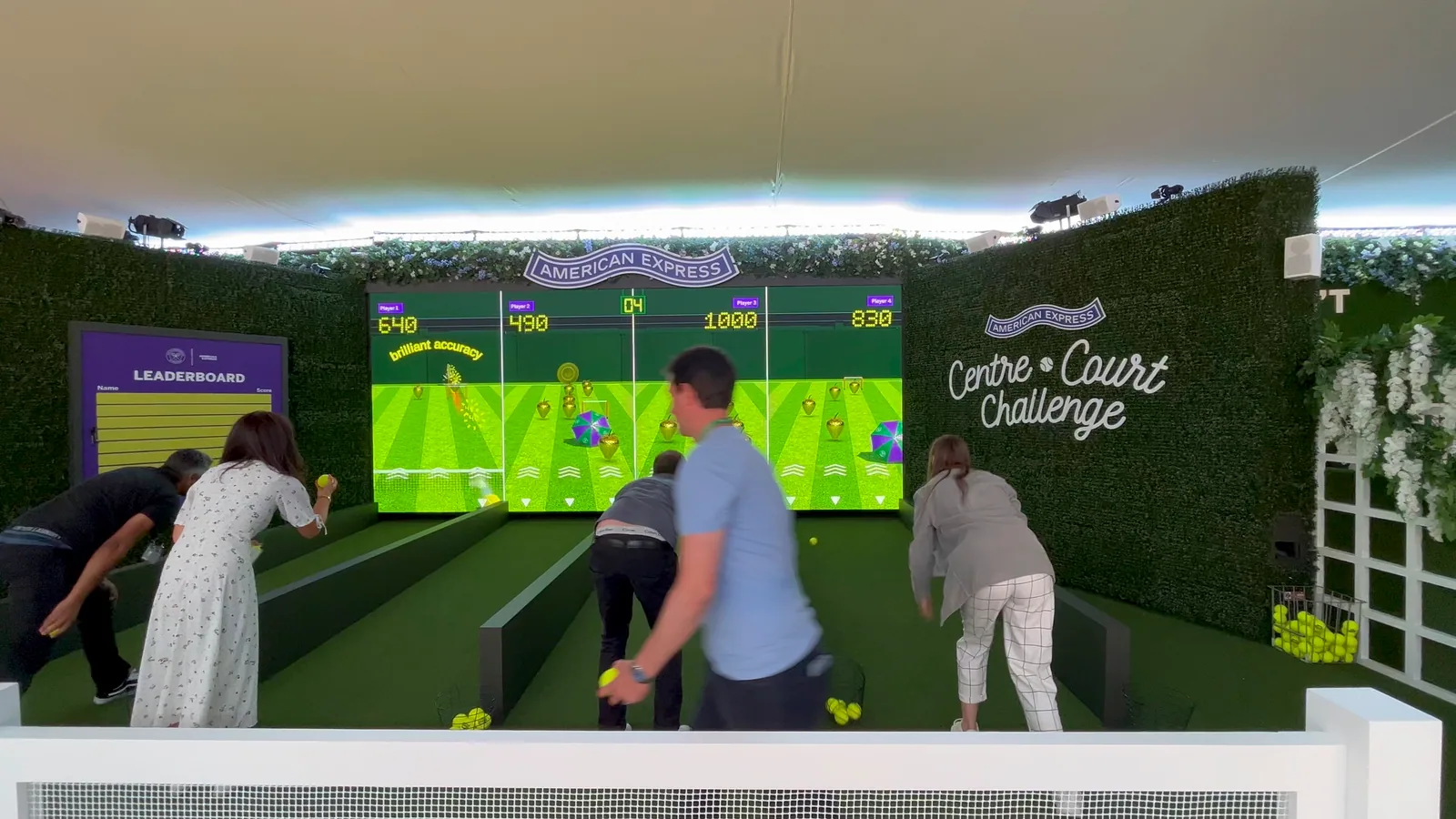 Four people mid-roll in the Centre Court Challenge lanes, scores showing above each lane