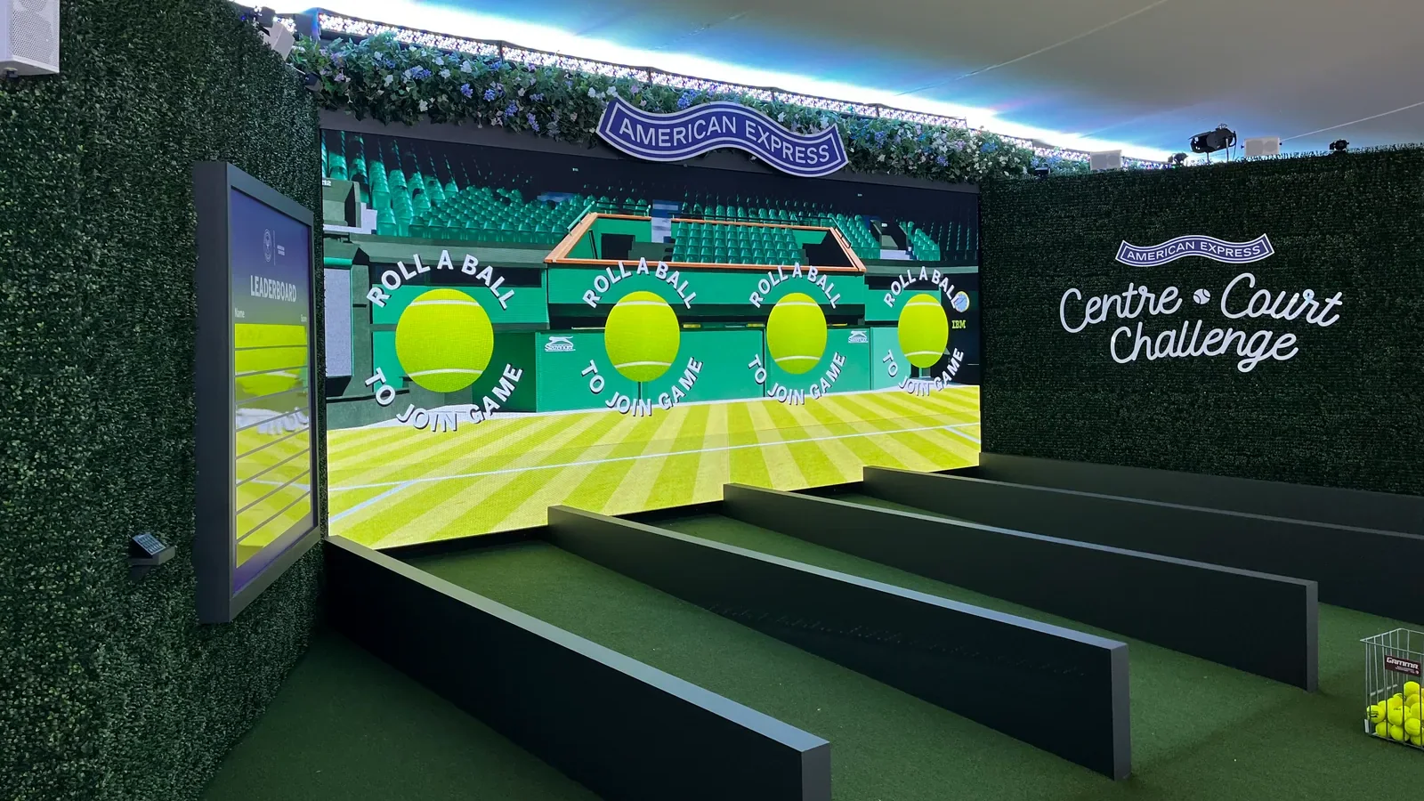 The Centre Court Challenge installation: four green lanes leading to a wide screen inviting players to roll a ball to join, with the game’s name on the hedge wall